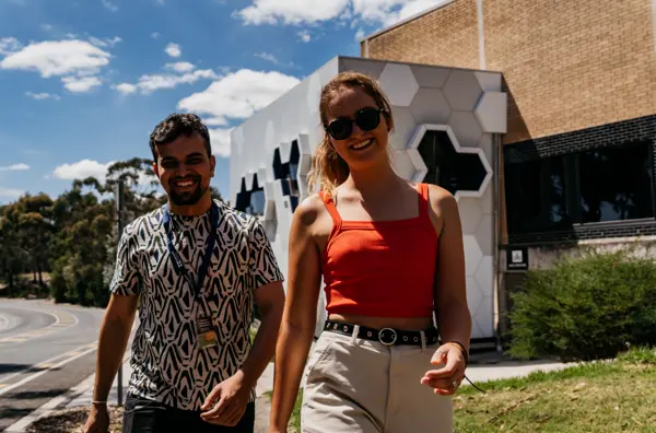 Photo of two young people walking outside on a sunny day.