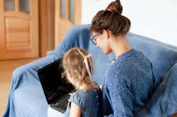 Photo of a mid twenties female and female child sitting on a sofa looking at a laptop computer.