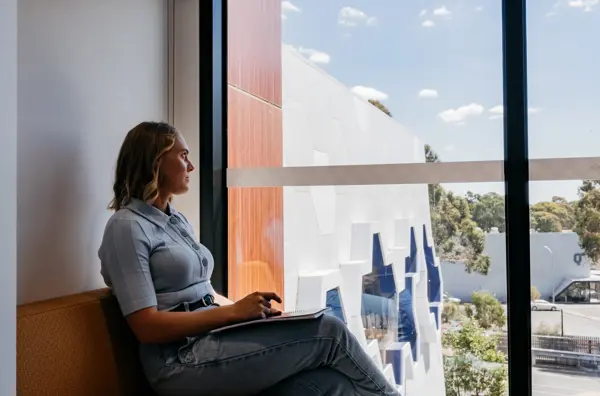 Photo of a person looking outside a window on a sunny day.