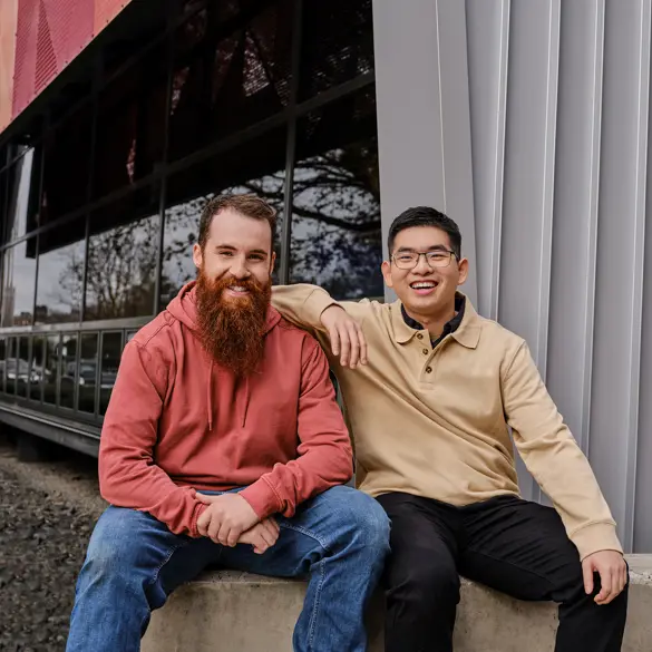 Photo of two people sitting closely on a concrete bench. One of the people has his right arm of the other persons shoulder.