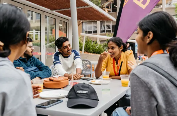 Photo of five people sitting at an outside table talking and eating.