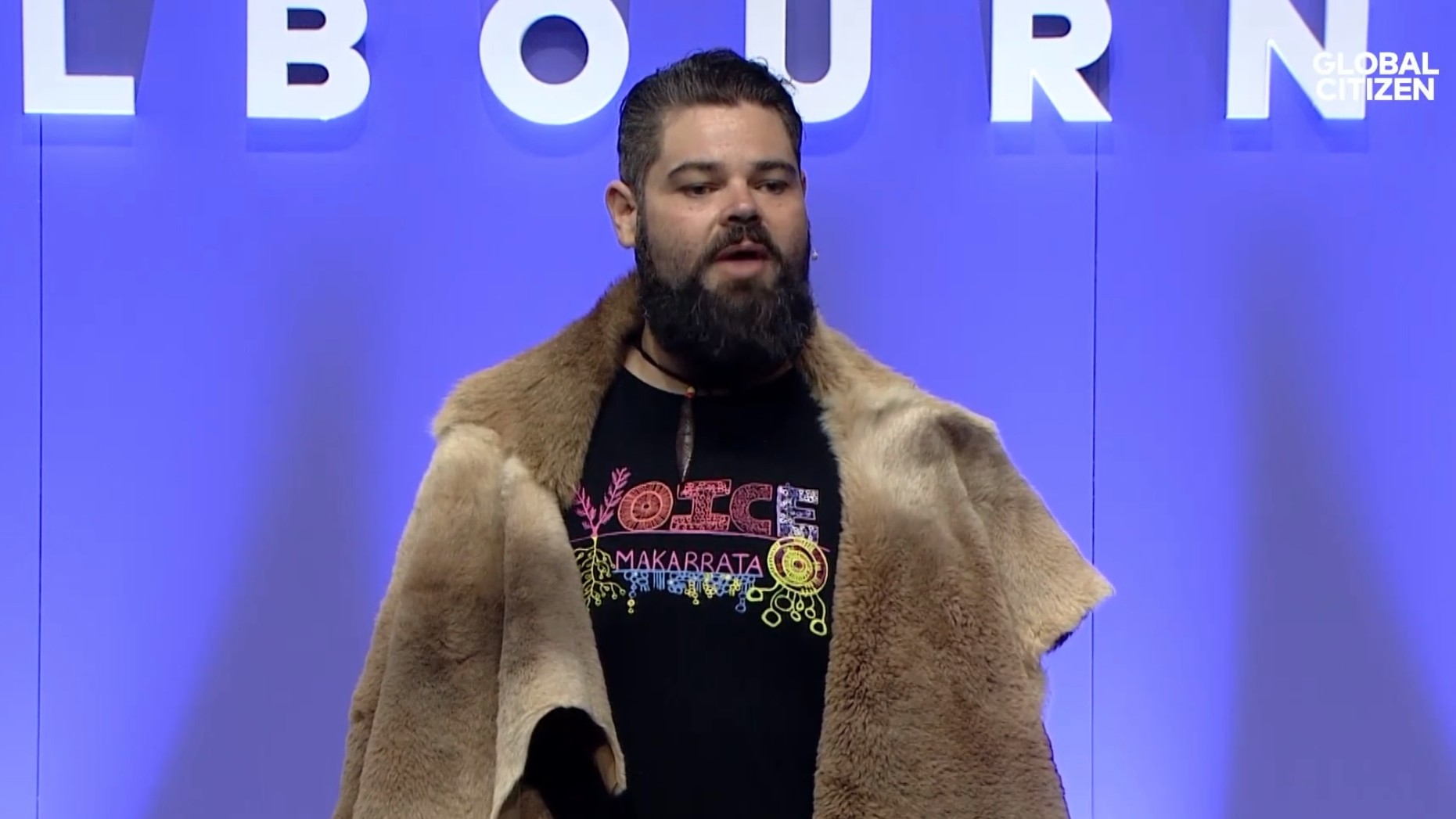 Indigenous man speaking in front of a Melbourne sign