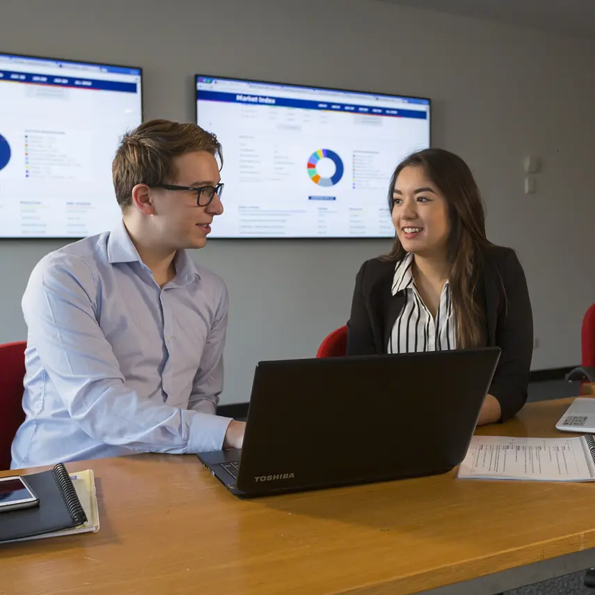 Two people sit at a table with a laptop open