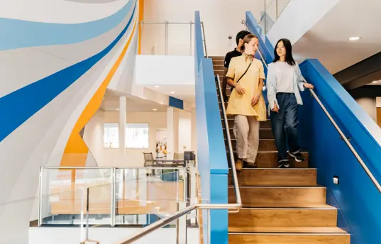 Photo of 3 people walking down a staircase in a modern looking building.