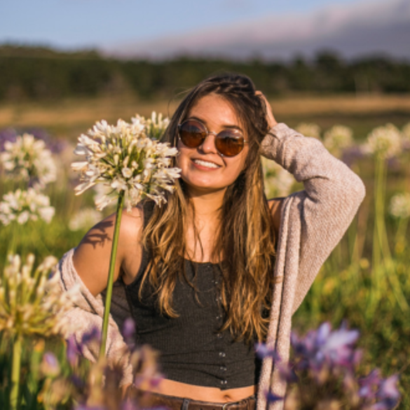 Photo of cool young girl wearing sunglasses standing in a sunny field of flowers.