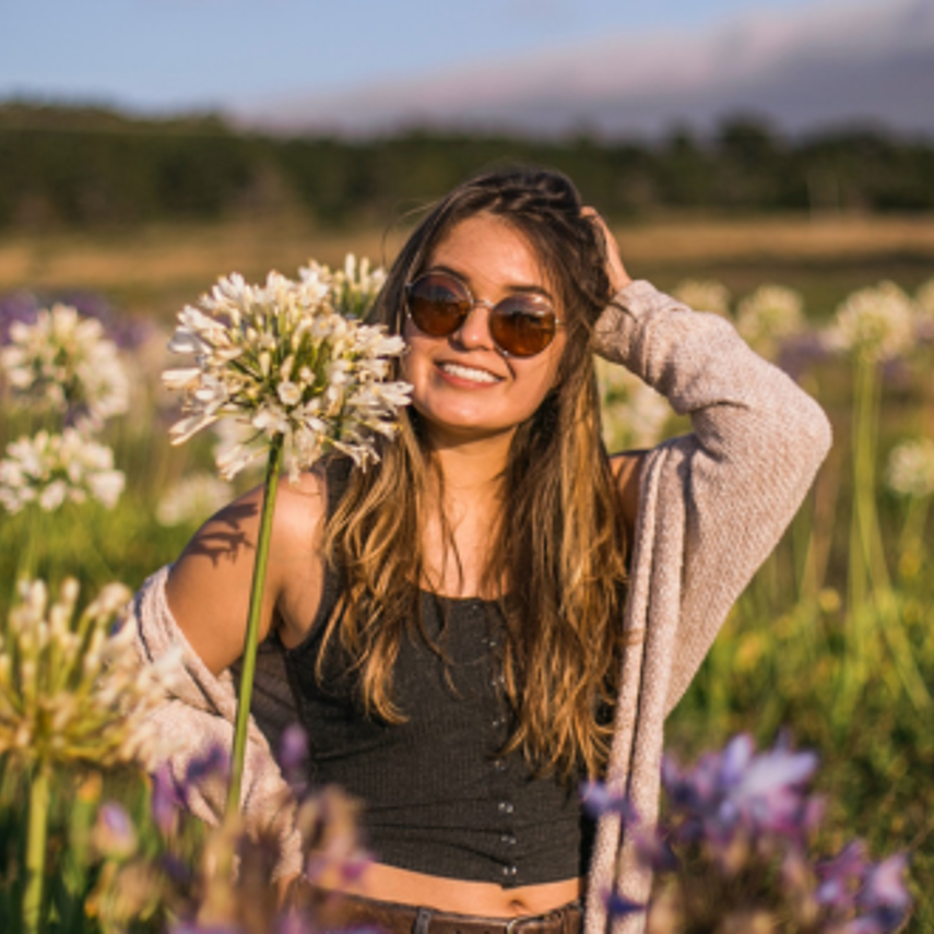 Photo of cool young girl wearing sunglasses standing in a sunny field of flowers.