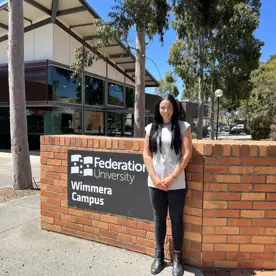 Photo of Danielle Taylor standing outside and in front of a Federation University Wimmera Campus sign.